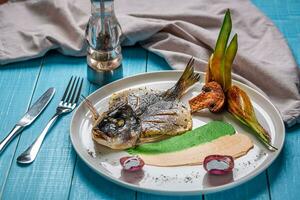 Fried fish dorado, decorated with cucumbers and onions. On a blue wooden background photo