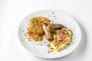 Grilled sausages, potatoes and braised cabbage on white plate close-up view from above. photo