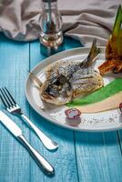 Fried fish dorado, decorated with cucumbers and onions. On a blue wooden background photo