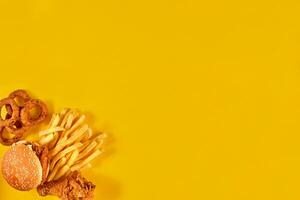 Fast food dish on yellow background. Fast food set fried chicken, meat burger and french fries. Take away fast food. photo