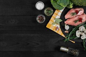 Cooking chicken breasts. On the table are spices - rosemary, red and black pepper, mushrooms, broccoli. Concept - healthy food. photo