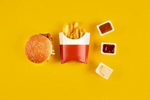 Fast food dish on yellow background. Fast food set meat burger, three sauce and french fries. Take away fast food. photo