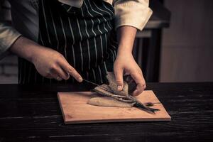 cocinero corte el pescado en un tablero foto