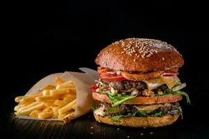 Cheese burger with grilled meat, cheese, tomato and potatoes on dark wooden surface. Ideal for advertisement. Close-up photo