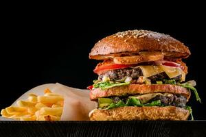 Cheese burger with grilled meat, cheese, tomato and potatoes on dark wooden surface. Ideal for advertisement. Close-up photo