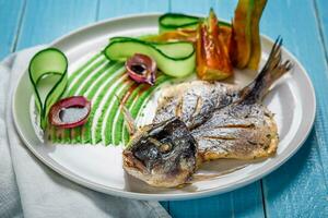 Fried fish dorado, decorated with cucumbers and onions. On a blue wooden background photo