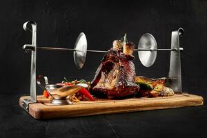 Roasted pork knuckle eisbein with braised boiled cabbage, potatoes, chili peppers and mustard on wooden cutting board, on a black background photo
