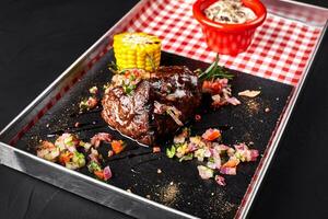 A piece of steak with salad, corn, mushrooms sauce on a blackboard photo