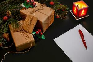 Christmas gifts and notebook lying near green spruce branch on black background top view. Space for text photo