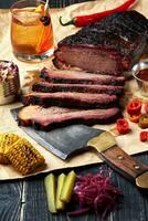 Fresh Brisket BBQ beef sliced for serving against a kraft paper background with sauce, hot peppers and corn. photo