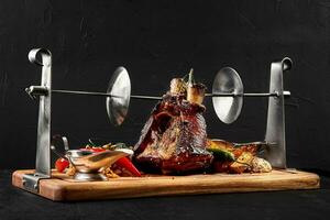 Roasted pork knuckle eisbein with braised boiled cabbage, potatoes, chili peppers and mustard on wooden cutting board, on a black background photo