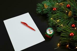 Red Christmas balls and notebook lying near green spruce branch on black background top view. Space for text photo