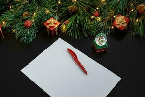 Christmas toys and notebook lying near green spruce branch on black background top view. Space for text photo