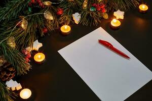 Red Christmas balls and notebook lying near green spruce branch on black background top view. Space for text photo