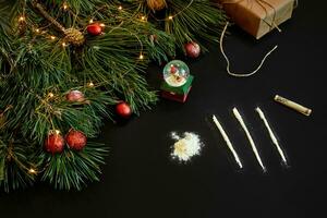 Cocaine divided into paths with Xmas toys and spruce branch on black background top view. photo