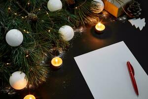 White Christmas balls and notebook lying near green spruce branch on black background top view. Space for text photo