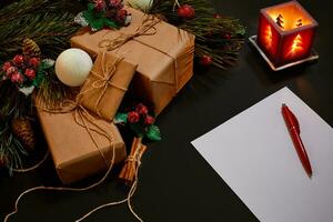 Christmas gifts and notebook lying near green spruce branch on black background top view. Space for text photo