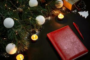White Christmas balls and notebook lying near green spruce branch on black background top view. Space for text photo