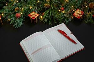 Christmas toys and notebook lying near green spruce branch on black background top view. Space for text photo