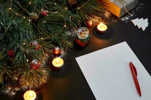 Red Christmas balls and notebook lying near green spruce branch on black background top view. Space for text photo