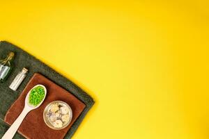 Spa or wellness setting in green colors. Bottles with essential aroma oil, towels, sea salt on yellow background. photo