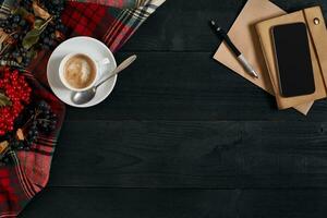 Smartphone with notebook and cup of coffee on wooden background. Cell phone with writing set with espresso photo