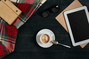 vacío tableta, un taza de café, cuaderno en el escritorio. tableta, taza caliente café en antiguo Clásico de madera tablero.arriba vista, plano laico foto