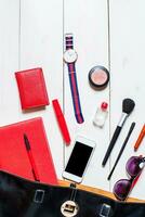 Cosmetics and women's accessories fell out of the black handbag on white background. photo