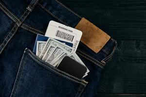 Dollars, smart, passport and plane ticket in your pocket jeans on black wooden background photo