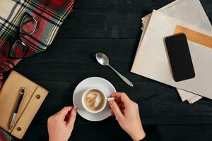 Newspaper and smartphone, reading glasses, notebook, hands holding coffee cup. photo