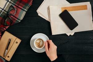 Newspaper and smartphone, reading glasses, notebook, hands holding coffee cup. photo