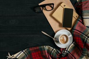 Above view of Smart phone with notebook and cup of latte coffee on black wooden background. photo