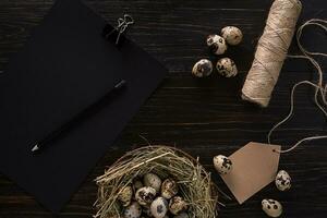 quail eggs in nest, notebook and thread on a black background photo