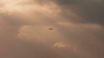 Dark silhouette of an airplane landing in the sun. Cloudy sunset. Jet plane approaching, long shot video