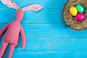 Easter background with eggs in nest and toy bunny on blue wooden background. Top view with copy space. photo