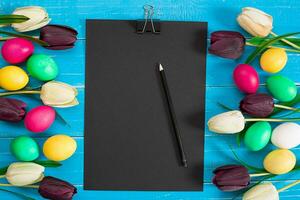 Colorful easter eggs and tulips on blue rustic wooden background photo
