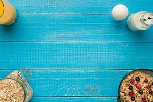 oat flakes with milk and berries bowl with spoon on blue wooden background, top view photo