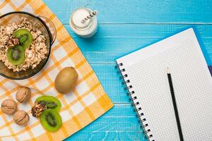 Bowl of fresh oatmeal porridge with kiwi and nuts on teal rustic table photo