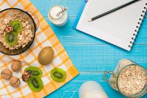 Bowl of fresh oatmeal porridge with kiwi and nuts on teal rustic table photo