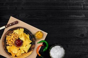 Lager beer and snacks on black wooden table. Nuts, chips. Top view with copyspace photo