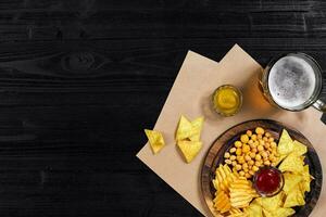 Lager beer and snacks on black wooden table. Nuts, chips. Top view with copyspace photo