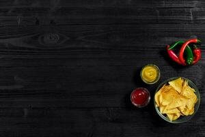 Glass plate with corn chips nachos and tomato sauce on a black wooden table top view. Place for text photo