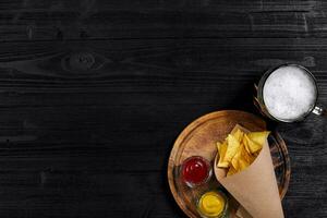 parte superior ver de tortilla papas fritas con salsa, vaso de cerveza en negro de madera antecedentes foto