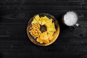 Lager beer and snacks on black wooden table. Nuts, chips. Top view with copyspace photo