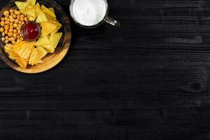 Lager beer and snacks on black wooden table. Nuts, chips. Top view with copyspace photo