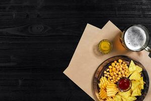 Lager beer and snacks on black wooden table. Nuts, chips. Top view with copyspace photo