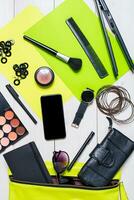 Cosmetics and women's accessories fell out of the green handbag on white background. photo