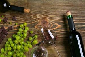 Red wine bottle, grape, chocolate and glasses over wooden table. Top view with copy space photo