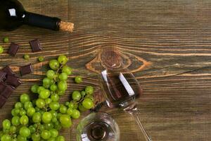 Red wine bottle, grape, chocolate and glasses over wooden table. Top view with copy space photo