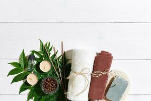 Spa set with towel and soap on white wooden background with green leaves photo